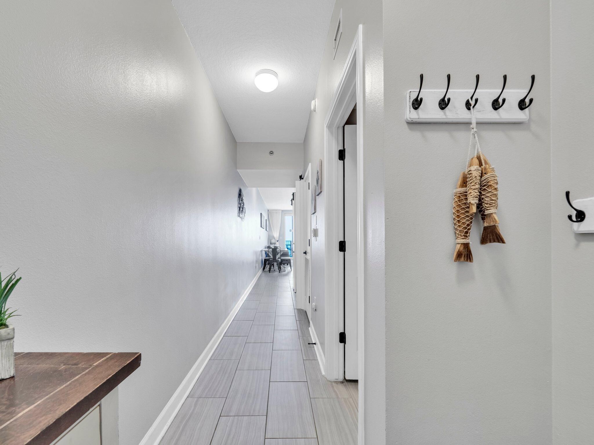 A hallway with a wooden bench, a plant, a wall-mounted hook with bags, and a ceiling light.