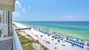 A beach with numerous umbrellas and people, a pier extending into the water, and a clear blue sky. - Shores of Panama 1002 (Panama City Beach)
