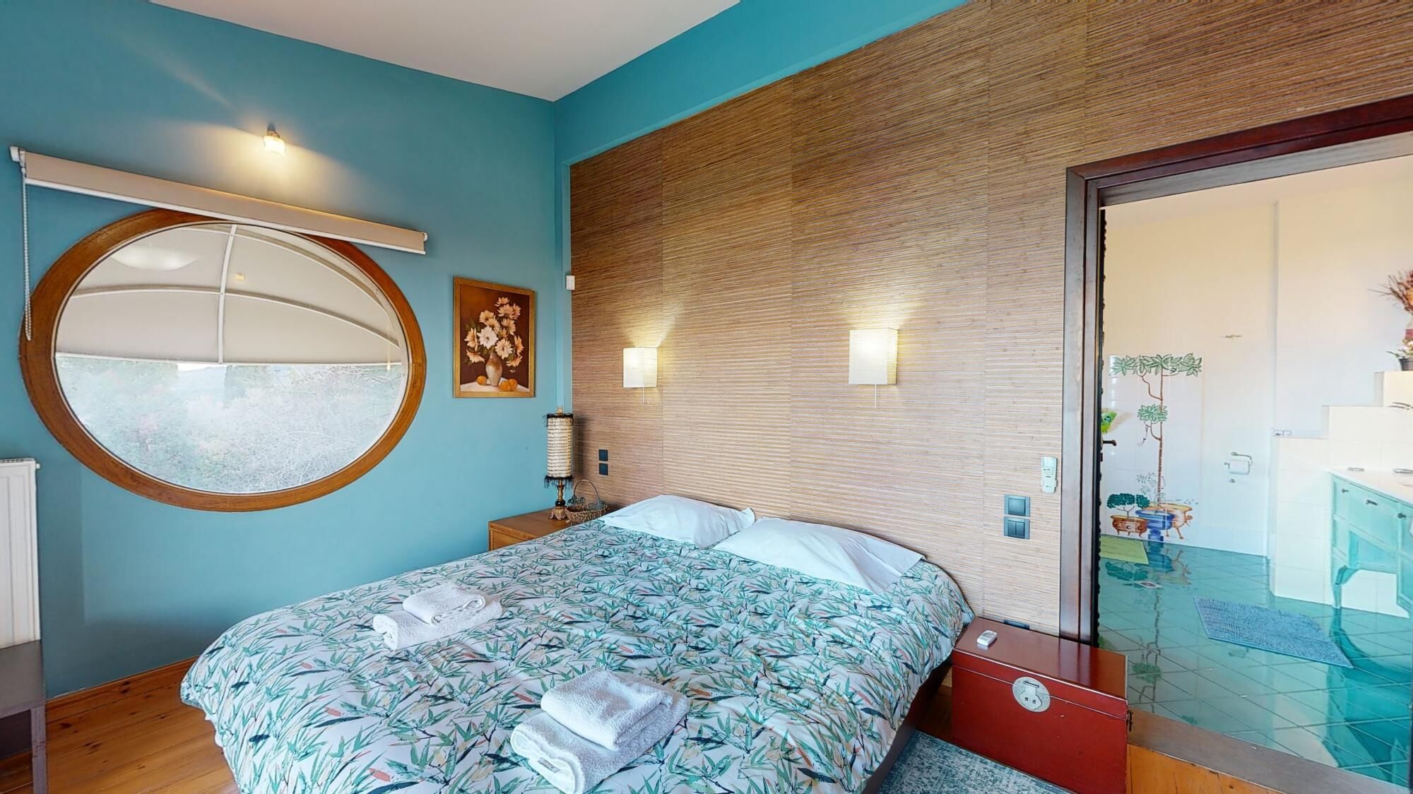 A bedroom with a bed, a round mirror, a wall-mounted lamp, and a wooden headboard.