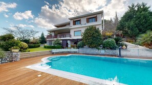 Relax by the villa's outdoor pool surrounded by a serene garden with a wooden deck and stone wall.