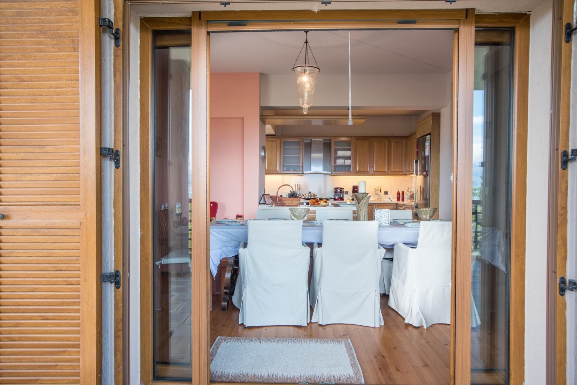 A modern kitchen with wooden cabinets, a dining area with white chairs, and a hanging light fixture.