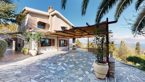 Una villa de estilo mediterráneo con patio de piedra, pérgola y vista al mar.