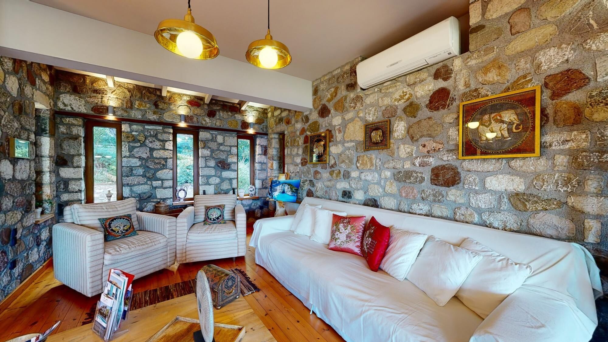 A cozy living room with a stone wall, white sofas, and a large window.