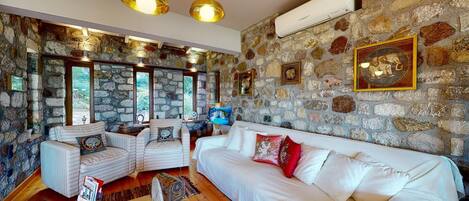 A cozy living room with a stone wall, white sofas, and a large window.