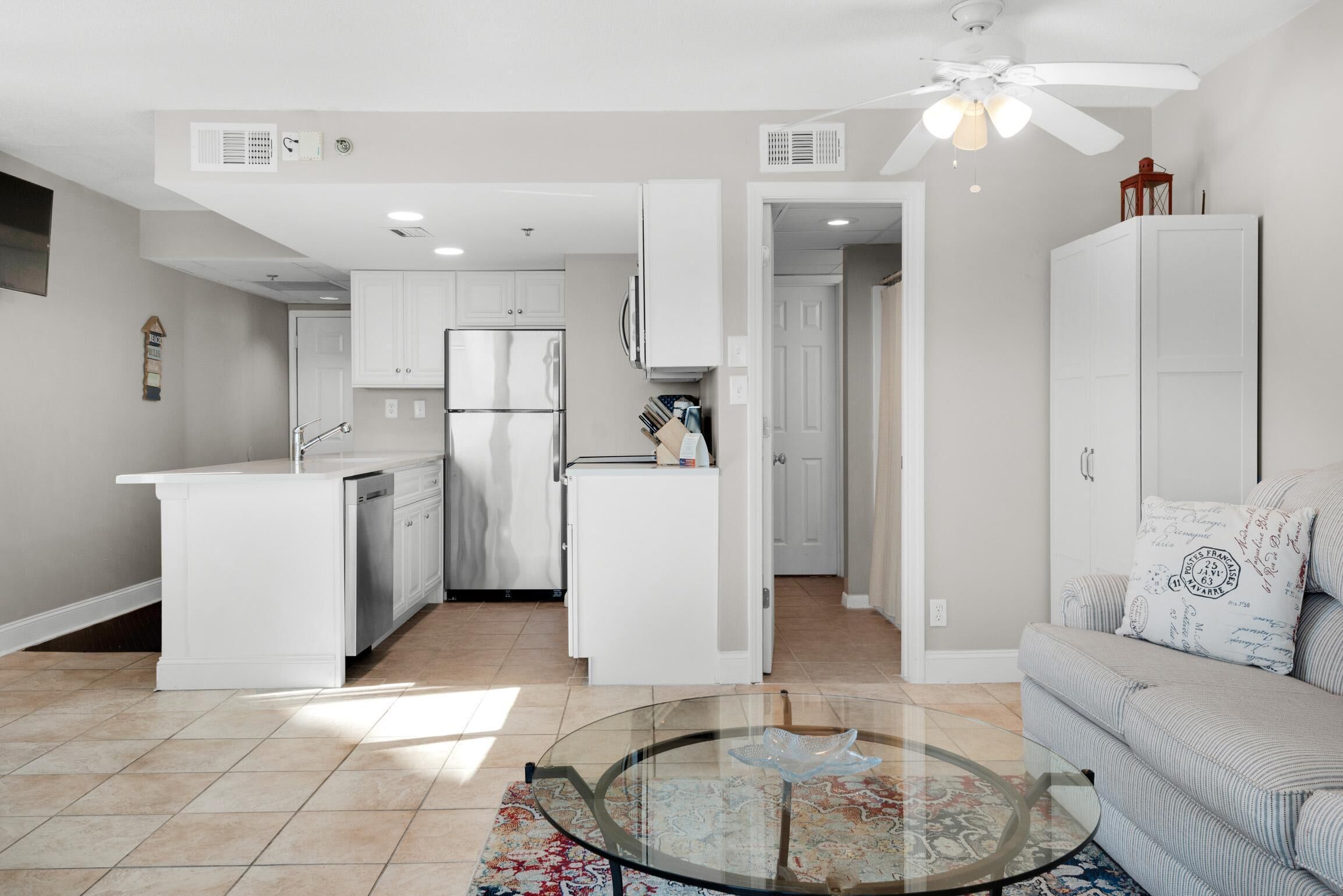 A modern kitchen with white cabinetry, a glass island, and a ceiling fan.