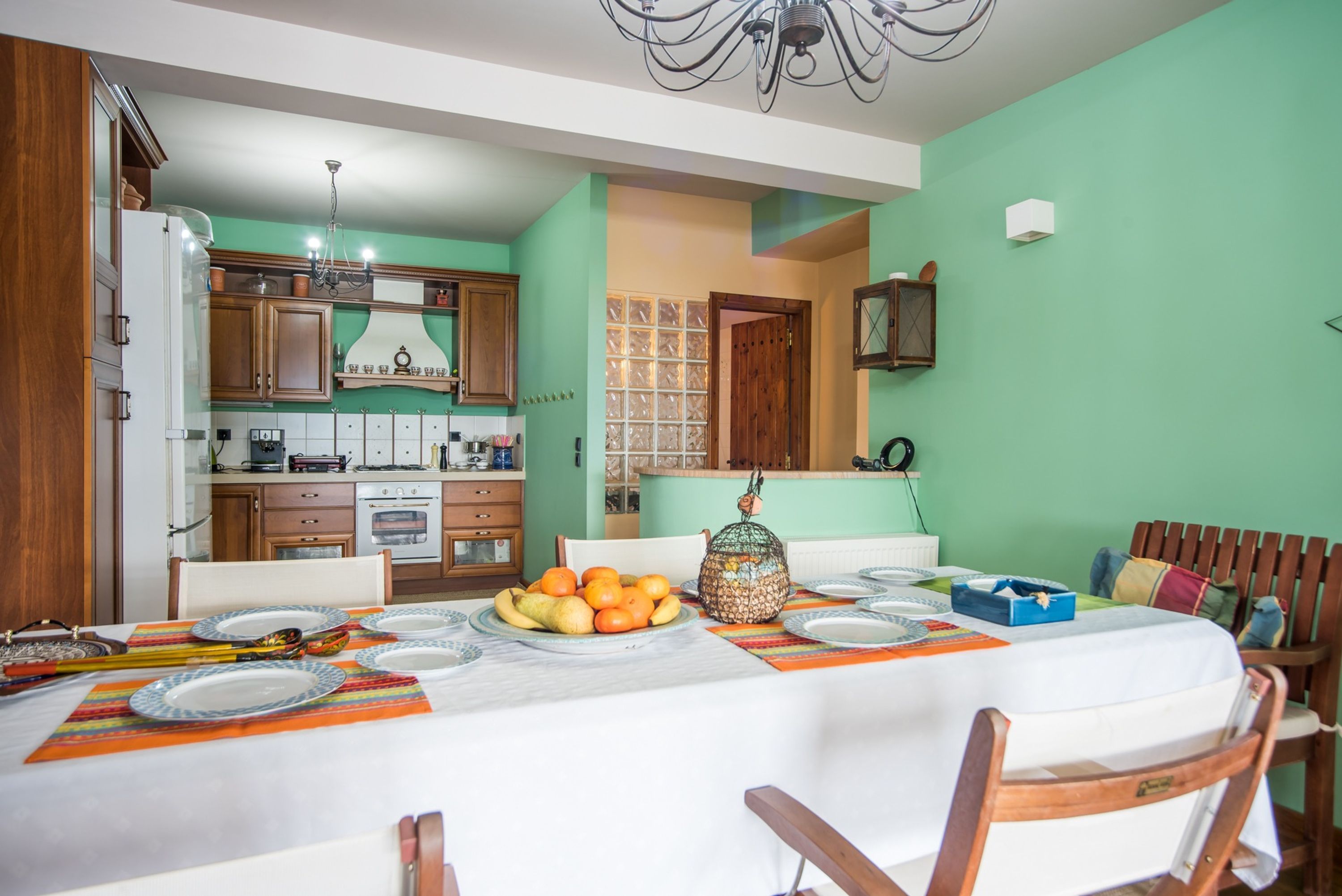 Un coin repas avec une table dressée pour quatre personnes, une cuisine en arrière-plan et un mur vert.