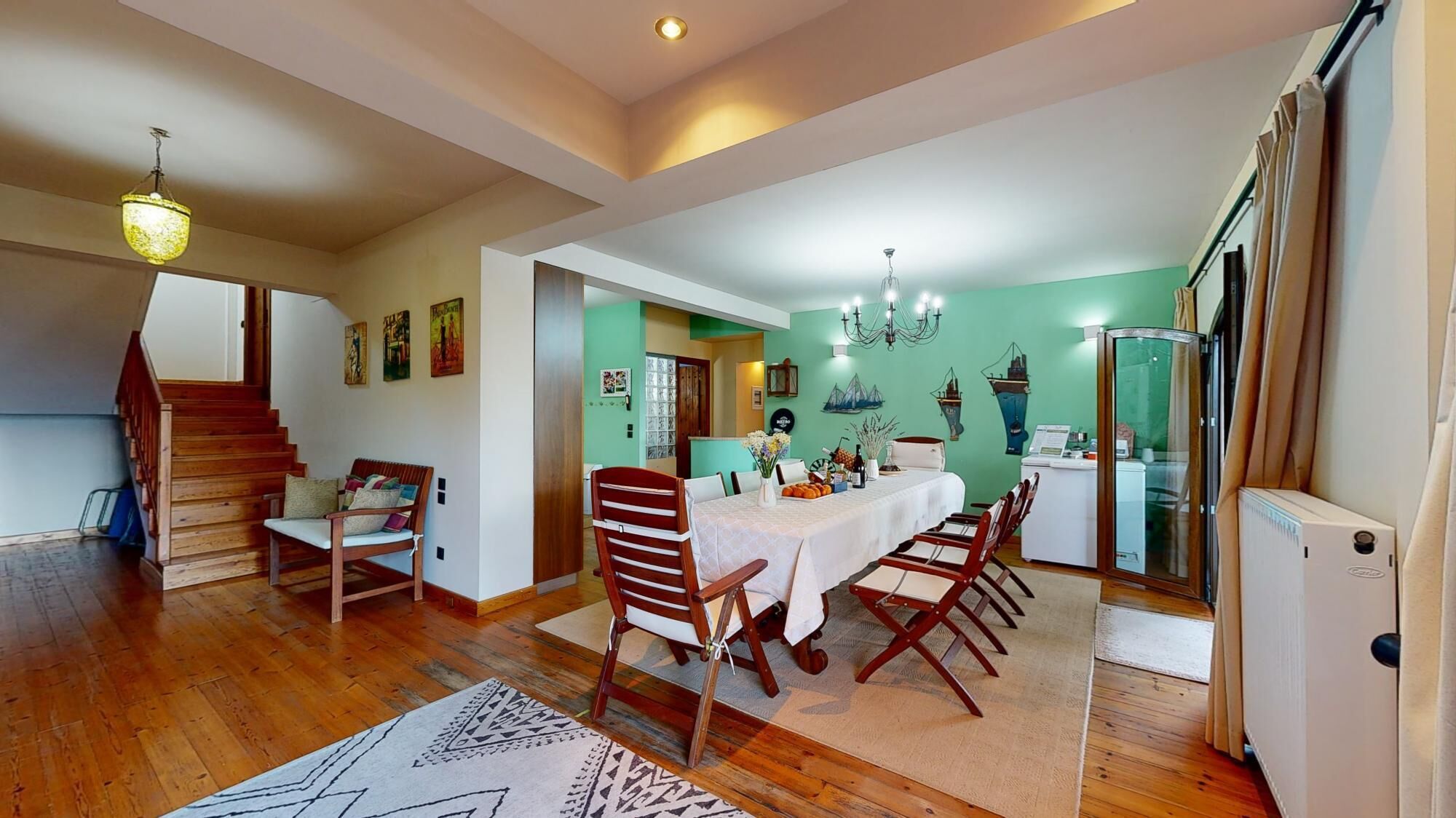 A spacious dining area with a wooden table and chairs, a staircase, and a kitchen area with a refrigerator and a washing machine.