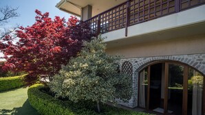 A two-story building with a stone facade, a balcony with a lattice design, and a large arched window. - Primavera Villa Sea View (Aigialeia)