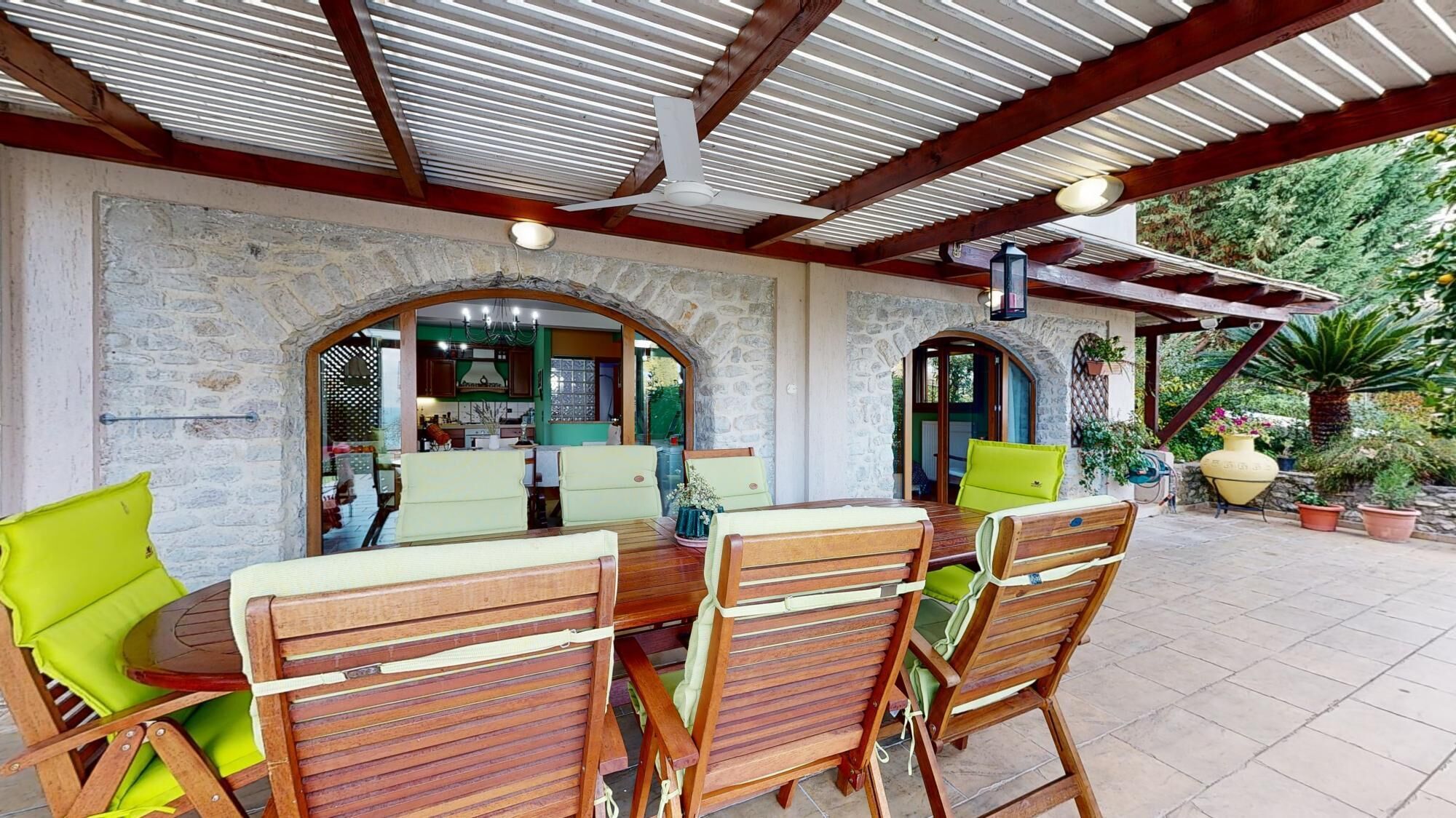An outdoor patio with a stone wall, wooden furniture, and a ceiling fan.
