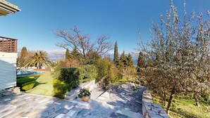 A stone patio with a pool, surrounded by various trees and shrubs. - Primavera Villa Sea View (Aigialeia)