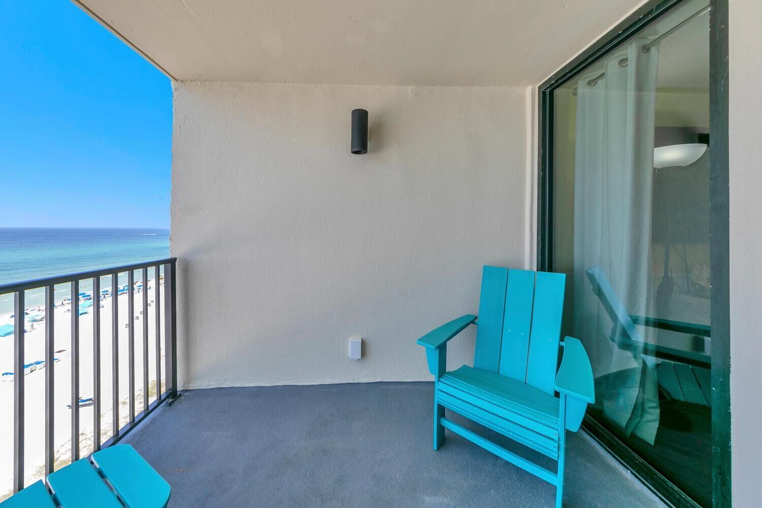 Un balcón con una silla turquesa, un vidrio y vista a la playa.