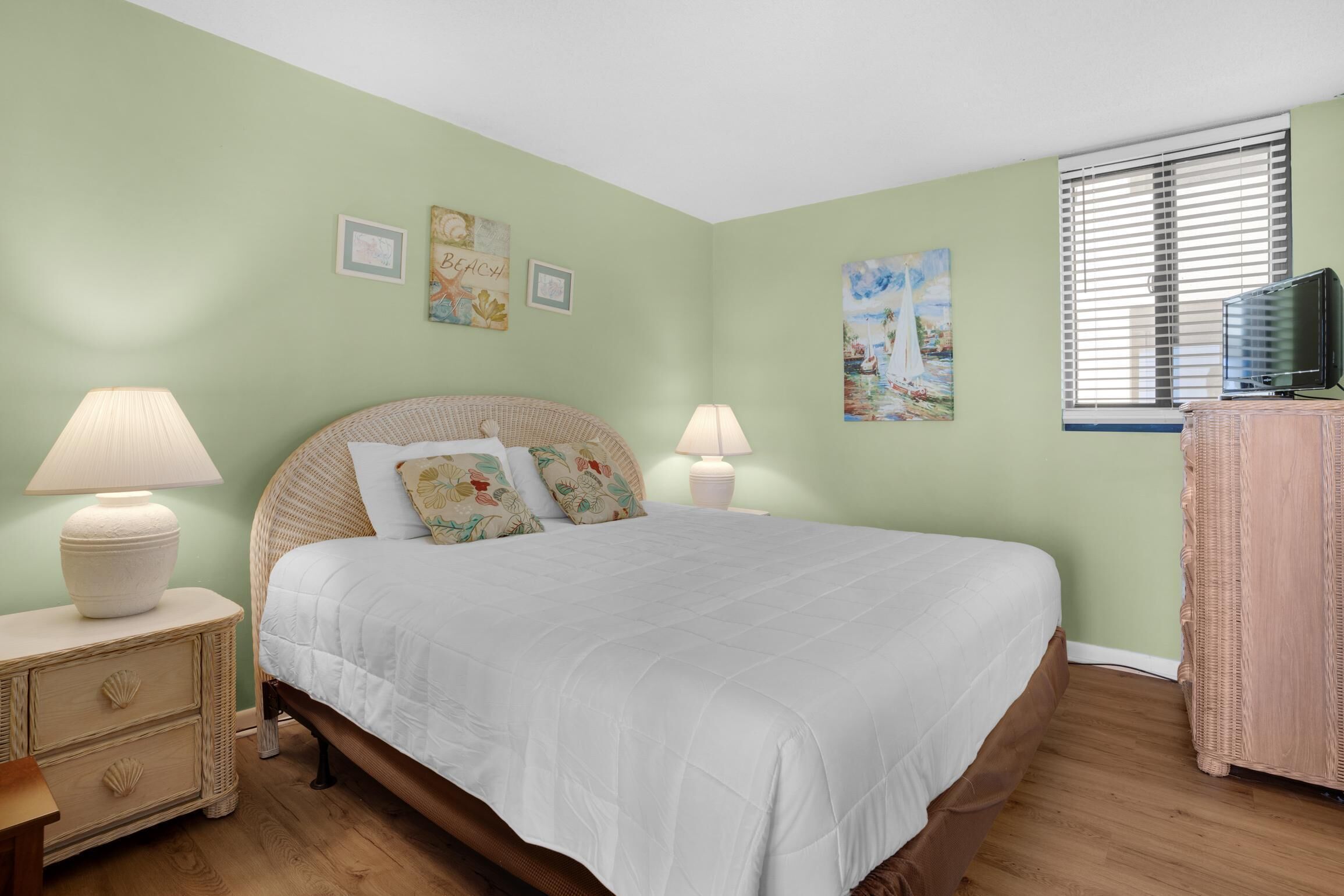 A bedroom with a bed, two bedside tables with lamps, a dresser, and wall art.