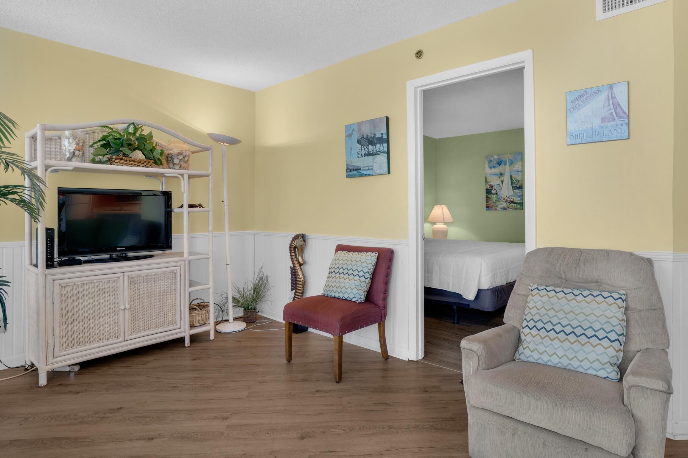 A living room with a television on a white cabinet, a red chair, a beige armchair, and a door leading to another room.