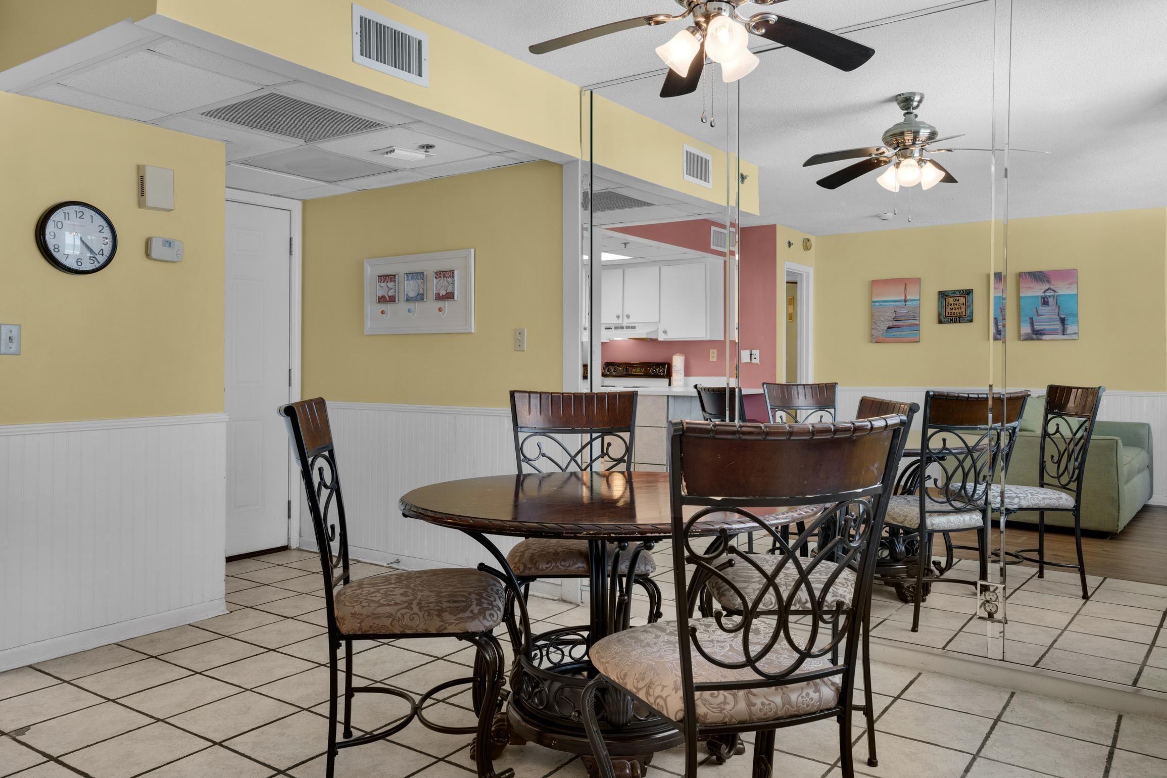 A dining area with a round table and chairs, a ceiling fan, and a clock on the wall.
