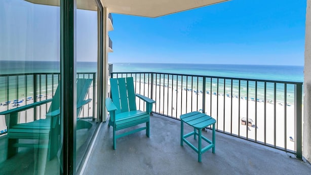 A balcony with a view of the beach, two green chairs, and a small table. - Sunbird 906w (Panama City Beach)
