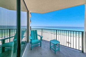 Un balcon donnant sur la plage, deux chaises vertes et une petite table.
