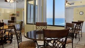 A dining area with a large round table and chairs, large windows with ocean views, and ceiling fans. - Sunbird 906w (Panama City Beach)