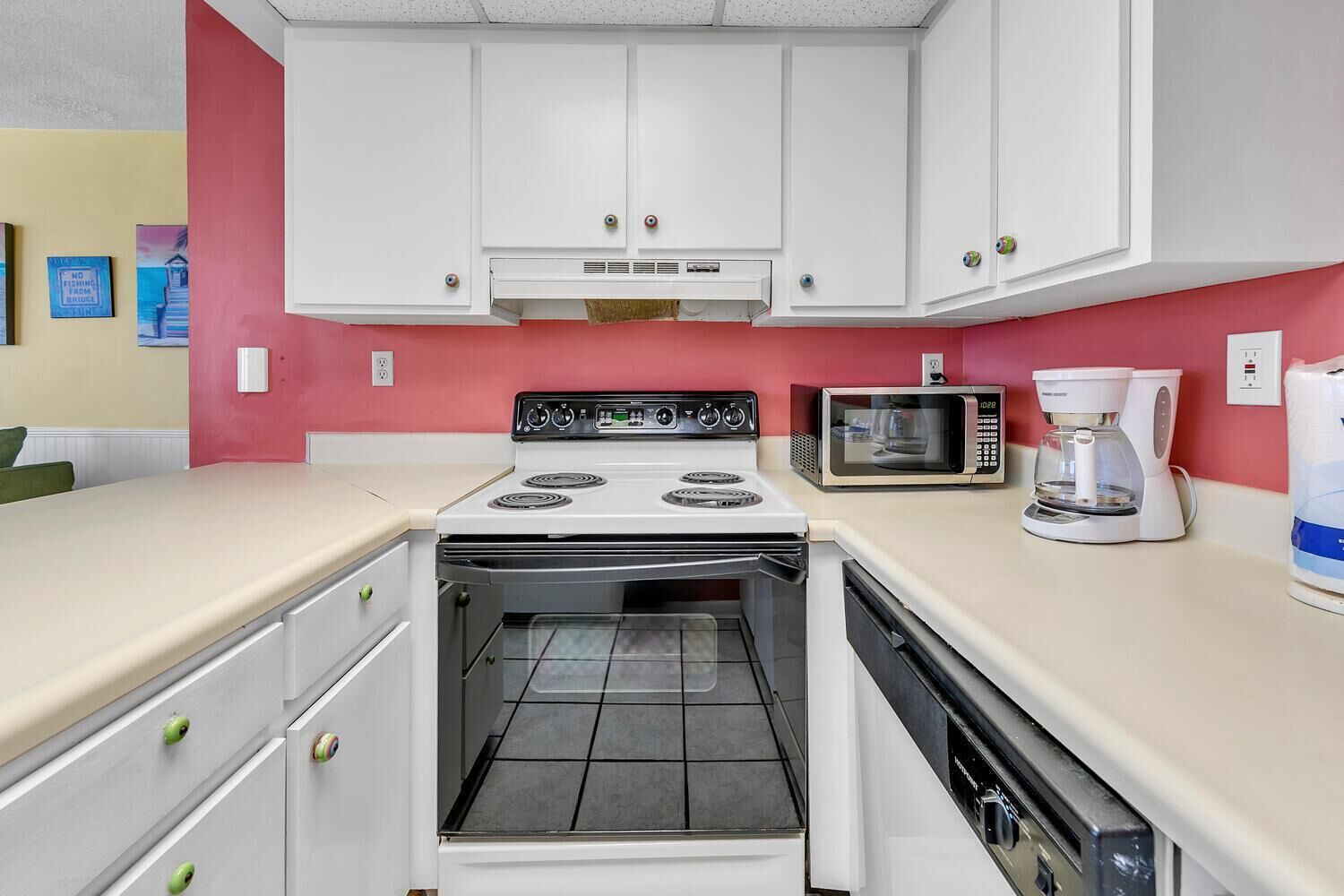 A compact kitchen with white cabinets, a stove, a microwave, and a coffee maker.