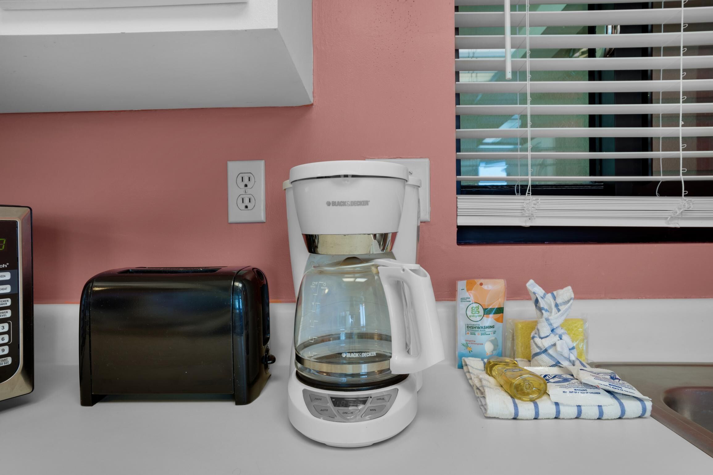 A kitchen with a toaster, a coffee maker, and some cleaning supplies on the counter.