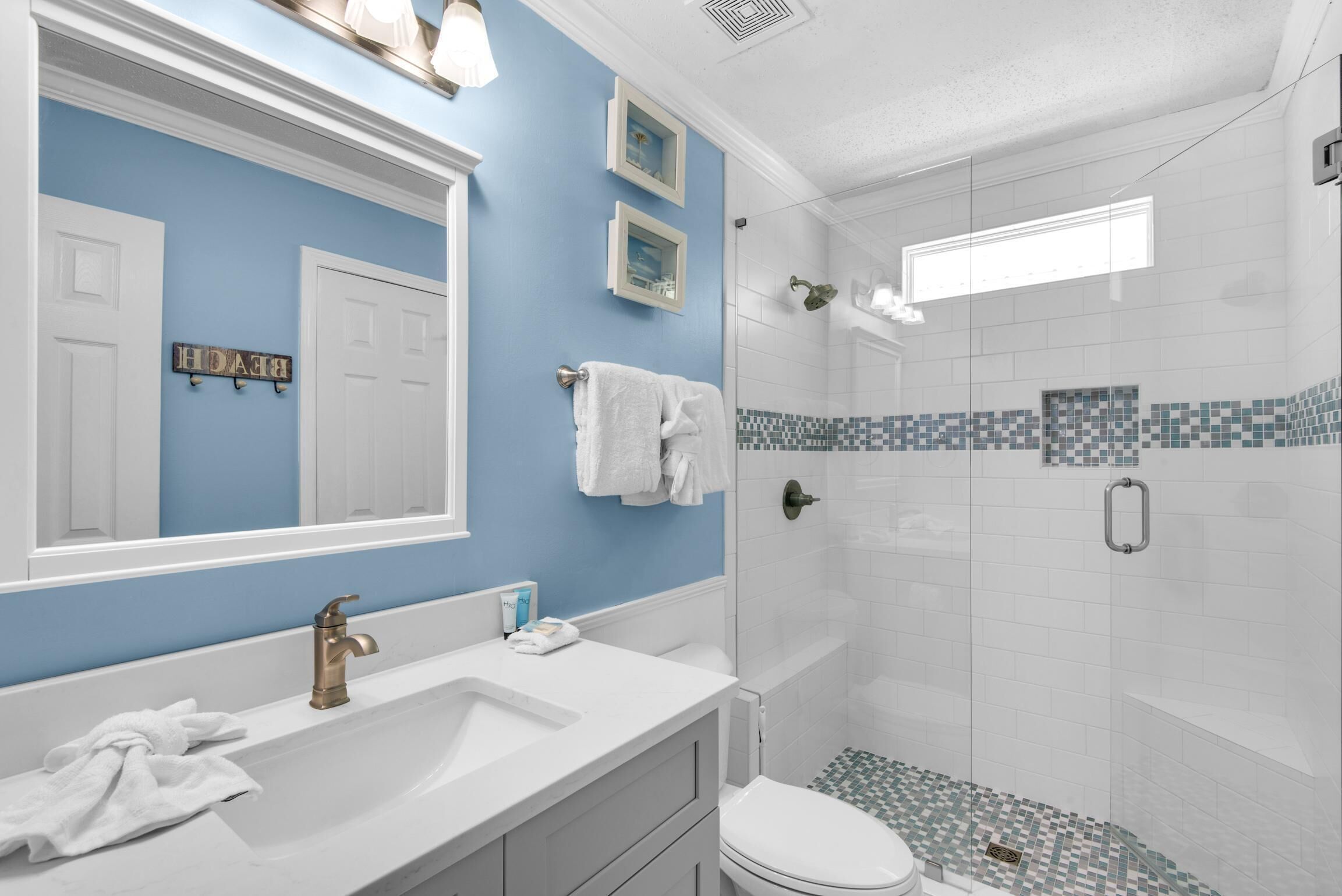 A bathroom with a blue accent wall, a white sink with a gold faucet, a white toilet, and a glass-enclosed shower area with a tiled floor.