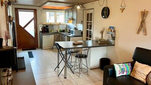 Une cuisine avec un coin repas, un canapé noir agrémenté d’un coussin coloré et un plafond en bois.