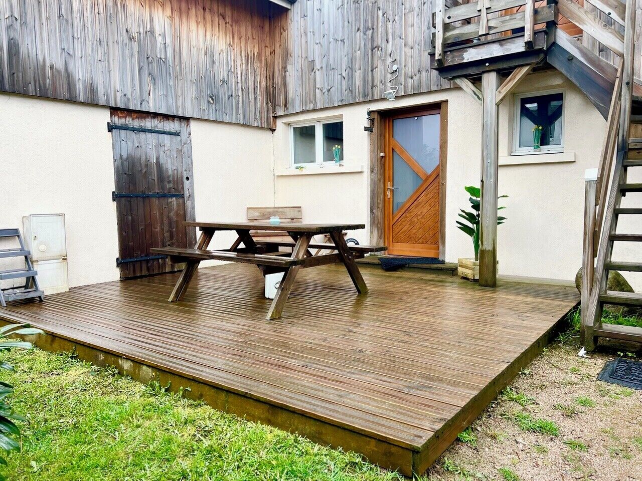 Une terrasse en bois avec une table de pique-nique, une porte en bois et une fenêtre ornée d’une plante.