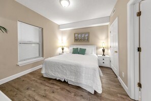 Relax in this serene bedroom with a large bed and a window with blinds, featuring a beautiful painting above.