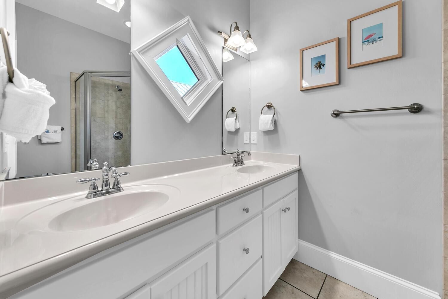 A bathroom with a large mirror, a white sink, and two framed pictures on the wall.