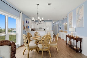 A dining area with a glass table, ornate chairs, a chandelier, and a view through large windows. - Riviera Dunes 203 (Pensacola)