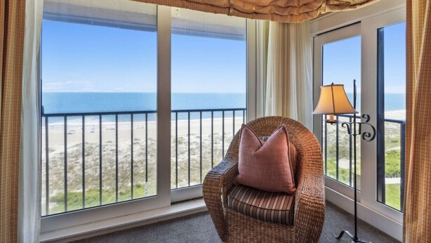 Un balcon avec un fauteuil en osier, une lampe et une vue sur la plage.