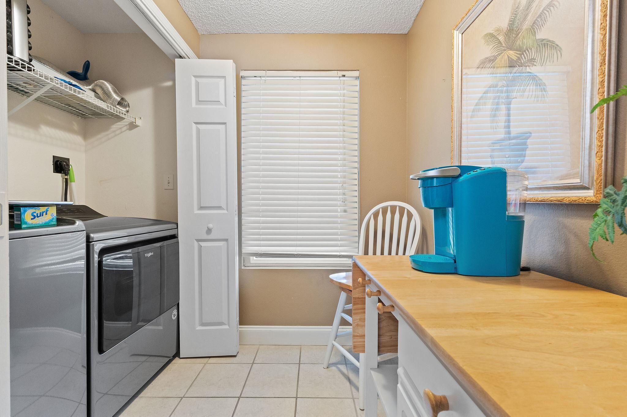 A compact kitchen with a washing machine, a coffee maker, and a chair.