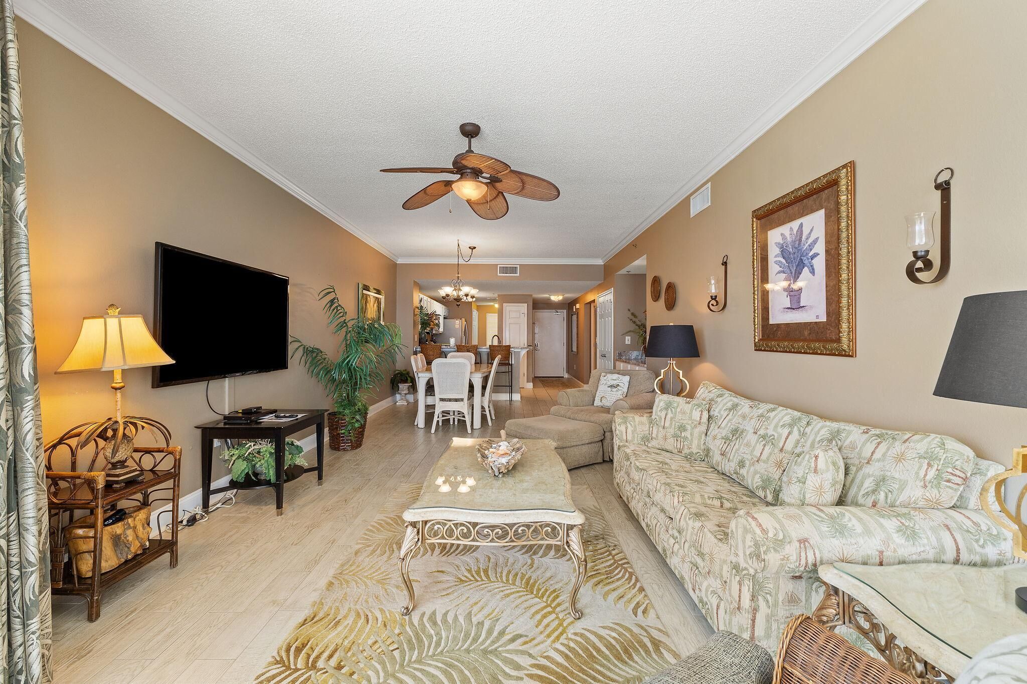 A living room with a ceiling fan, a flat-screen TV, a sofa, a coffee table, and a dining area in the background.