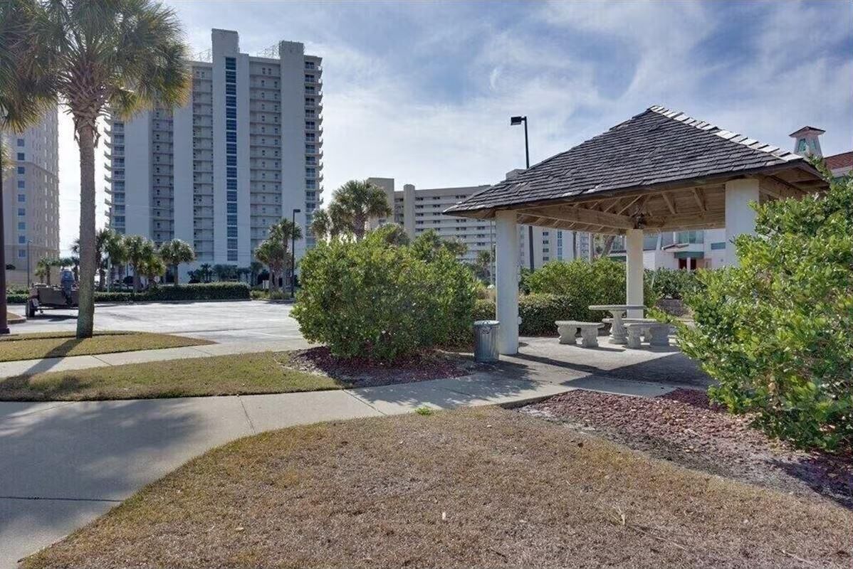 A park area with a gazebo, palm trees, and a building in the background.