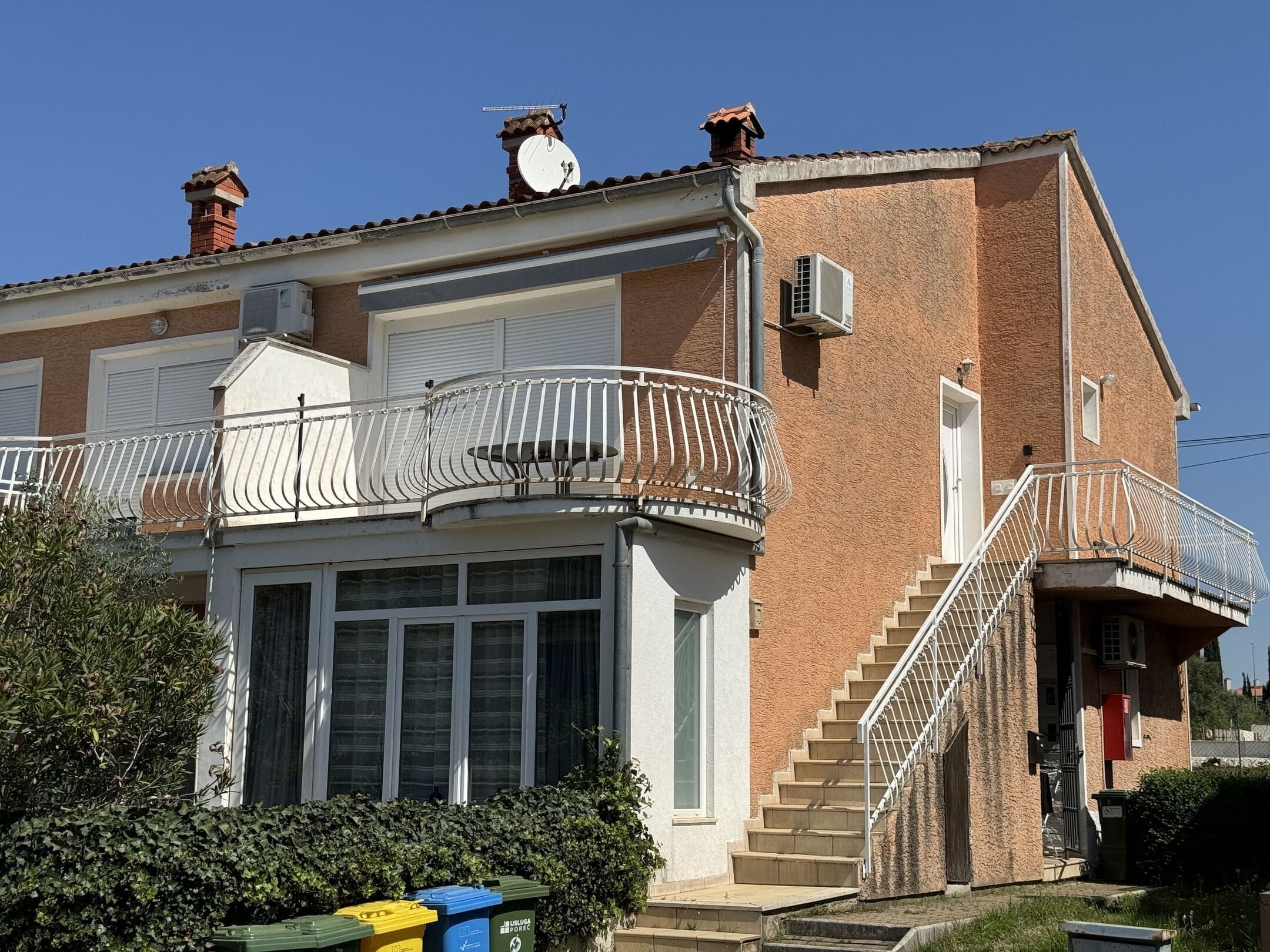 Un edificio de dos pisos con un balcón, una escalera y una puerta de garaje.