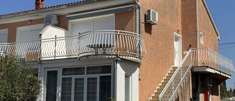 Un edificio de dos pisos con un balcón, una escalera y una puerta de garaje.