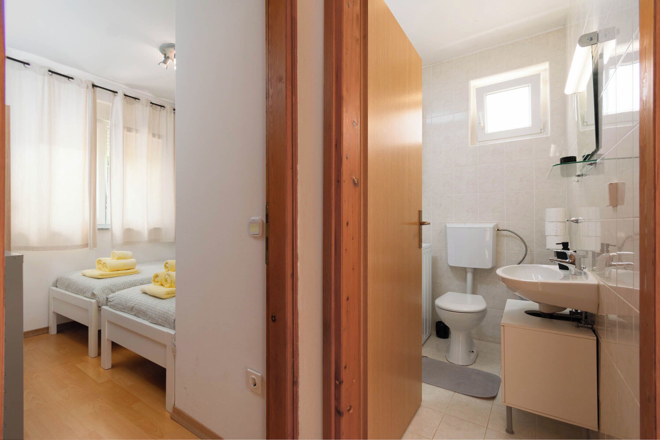 A bedroom with two beds, a bathroom with a sink and toilet, and a window with curtains.