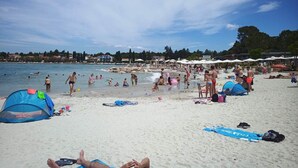Una playa con gente nadando y tomando el sol, tiendas de campaña y sombrillas.