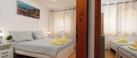 Quarto com cama, mesas de cabeceira, luminária, janela com cortinas e um quadro na parede.