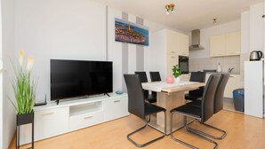 Una cocina moderna con armarios blancos, una mesa de comedor con sillas, un televisor de pantalla plana y un cuadro en la pared.