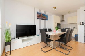 Una cocina moderna con armarios blancos, una mesa de comedor con sillas, un televisor de pantalla plana y un cuadro en la pared.