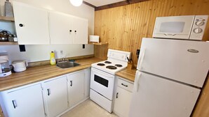Eine kleine Küche mit weißen Schränken, einem Herd, einem Spülbecken und einem Kühlschrank.