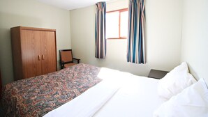 Ein Schlafzimmer mit einem Bett, einem Holzschrank, einem Sessel und einem Fenster mit Vorhängen.