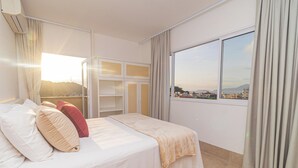 A hotel room with a bed, a large window with curtains, and a view of the cityscape. - Vossa Bossa Ubatuba Acarau (Ubatuba)