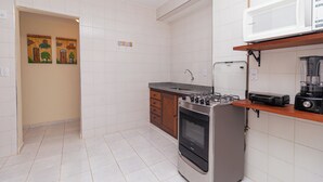 A kitchen with white tiles, a built-in oven, a microwave, and a blender on the countertop. - Vossa Bossa Ubatuba Acarau (Ubatuba)