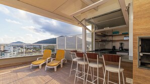 A balcony with a view of the city, a kitchen area, and seating with a view. - Vossa Bossa Ubatuba Acarau (Ubatuba)