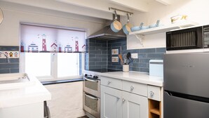 Una cocina con horno doble, microondas y refrigerador. Hay una ventana con vista a casas y una puerta con manija.