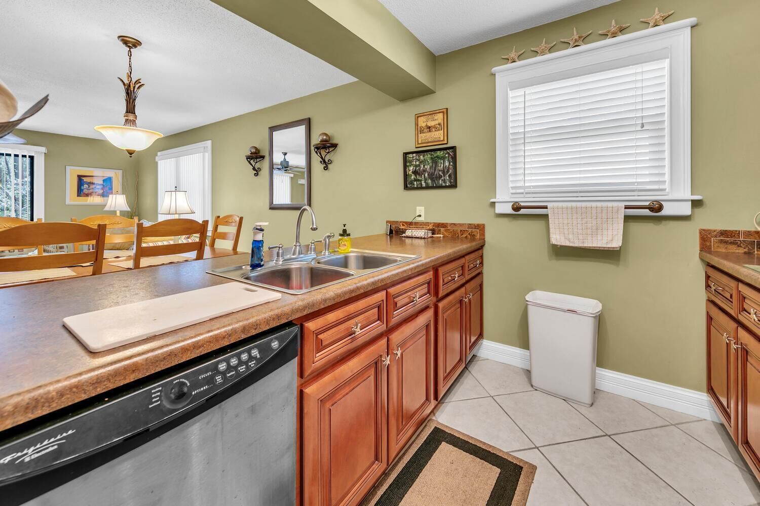 A kitchen with wooden cabinets, a dishwasher, a sink, and a window with blinds.