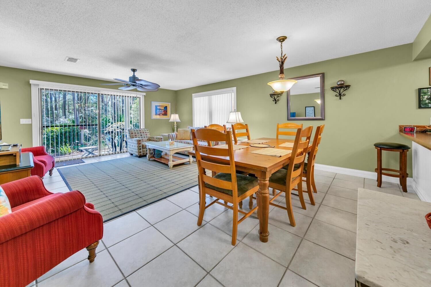 A dining area with a wooden table and chairs, a ceiling fan, and a view of the outdoors through large windows.