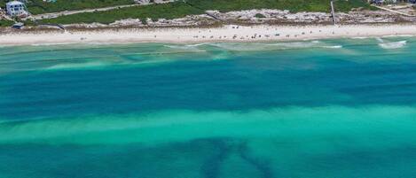 Oversigtsbillede af et kystområde med strand, huse og klart turkis vand.