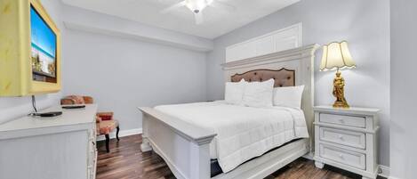 Un dormitorio con cama, mesita de noche, lámpara, televisión y ventilador de techo.
